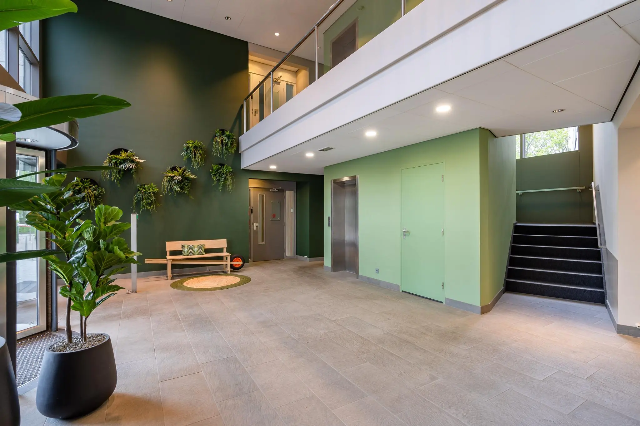 Moderne, groene entreehal aan de Baarnsche Dijk met plantenwand, houten bank en trap naar de bovenverdieping.